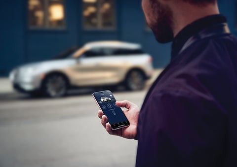A person is shown interacting with a smartphone to connect to a Lincoln vehicle across the street. | Bergstrom Lincoln of Neenah in Neenah WI