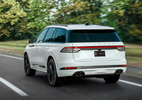 A white 2025 Lincoln Aviator® SUV is being driven away down a road lined with colorful trees. | Bergstrom Lincoln of Neenah in Neenah WI