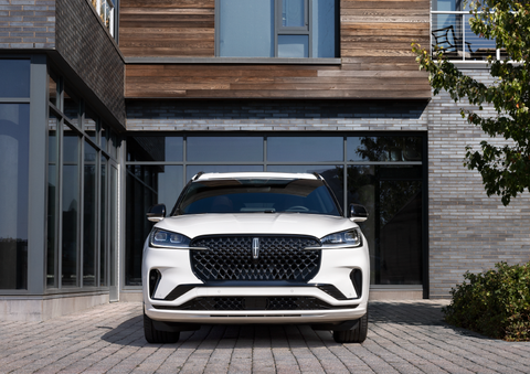 A white 2025 Lincoln Aviator® SUV is shown parked outside a modern building with gray brick and wood accents. | Bergstrom Lincoln of Neenah in Neenah WI