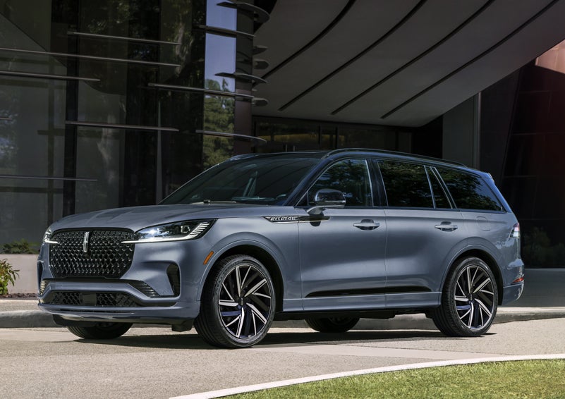 A gray 2025 Lincoln Aviator® SUV is parked outside a modern building showcasing the driver’s side of the vehicle. | Bergstrom Lincoln of Neenah in Neenah WI