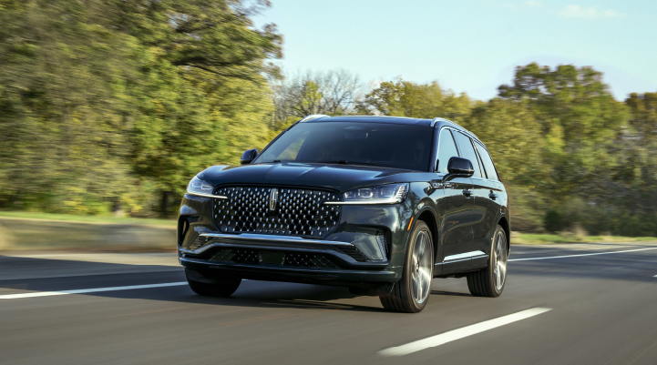 A 2025 Lincoln Black Label Aviator® SUV is being driven down a road lined with trees. | Bergstrom Lincoln of Neenah in Neenah WI