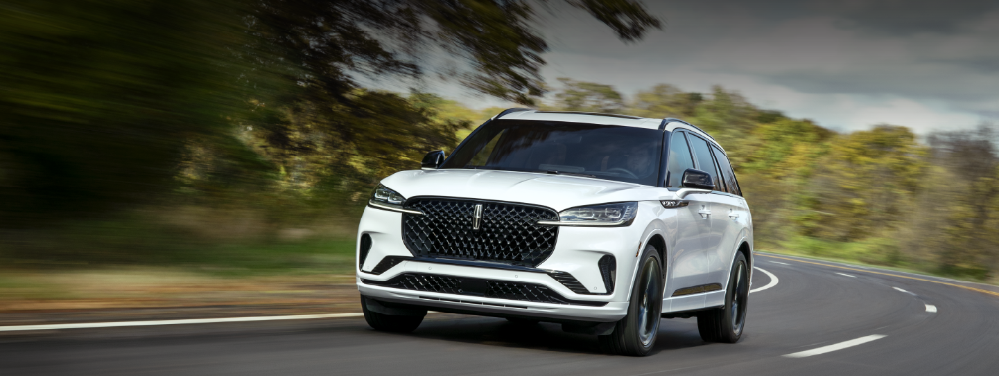 A white 2025 Lincoln Aviator® SUV is being driven down a road lined with trees. | Bergstrom Lincoln of Neenah in Neenah WI