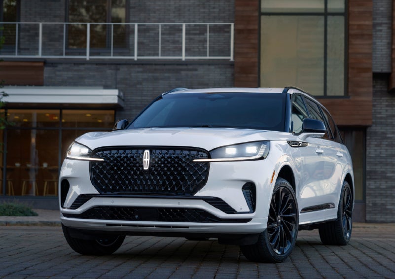 A 2026 Lincoln Aviator® Reserve model is shown with the available Jet Appearance Package parked near a restaurant. | Bergstrom Lincoln of Neenah in Neenah WI