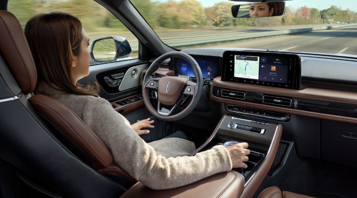 A 2026 Lincoln Aviator® SUV is being driven hands-free on a highway near a forest | Bergstrom Lincoln of Neenah in Neenah WI