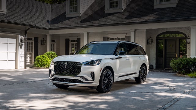 A white 2026 Lincoln Aviator® SUV is parked in the driveway of a luxury home. | Bergstrom Lincoln of Neenah in Neenah WI