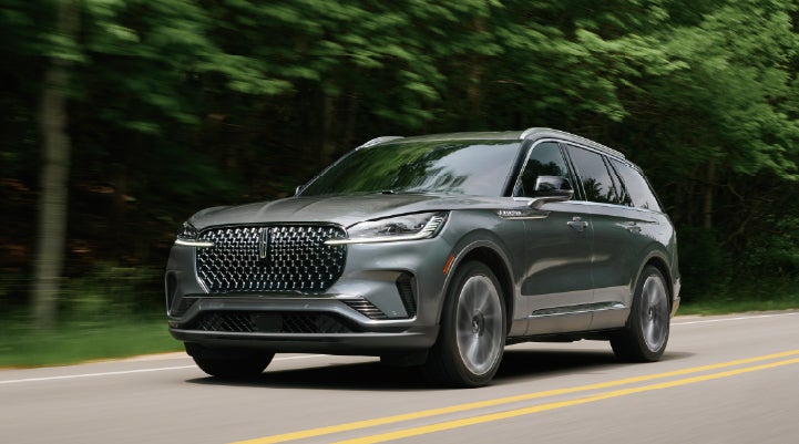 A 2027 Lincoln Aviator® SUV is being driven down a road lined with trees. | Bergstrom Lincoln of Neenah in Neenah WI